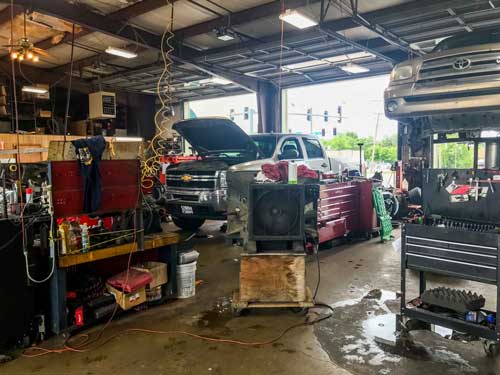 A car is being worked on in a garage with the hood up.