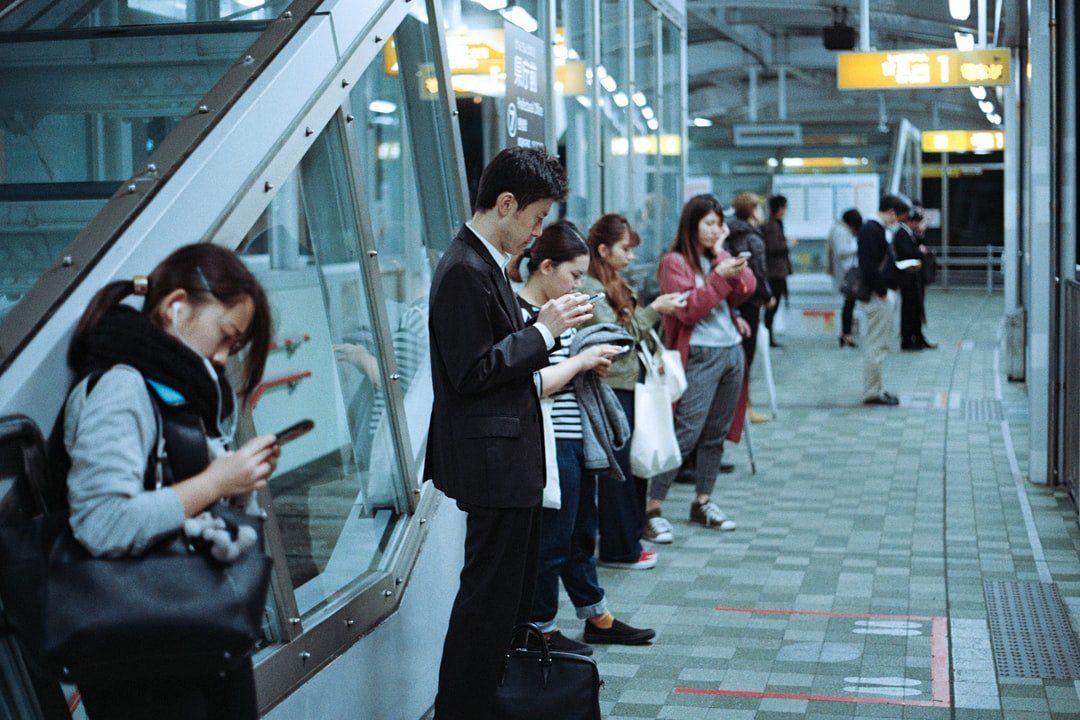 A group of people are standing on a train platform looking at their phones.
