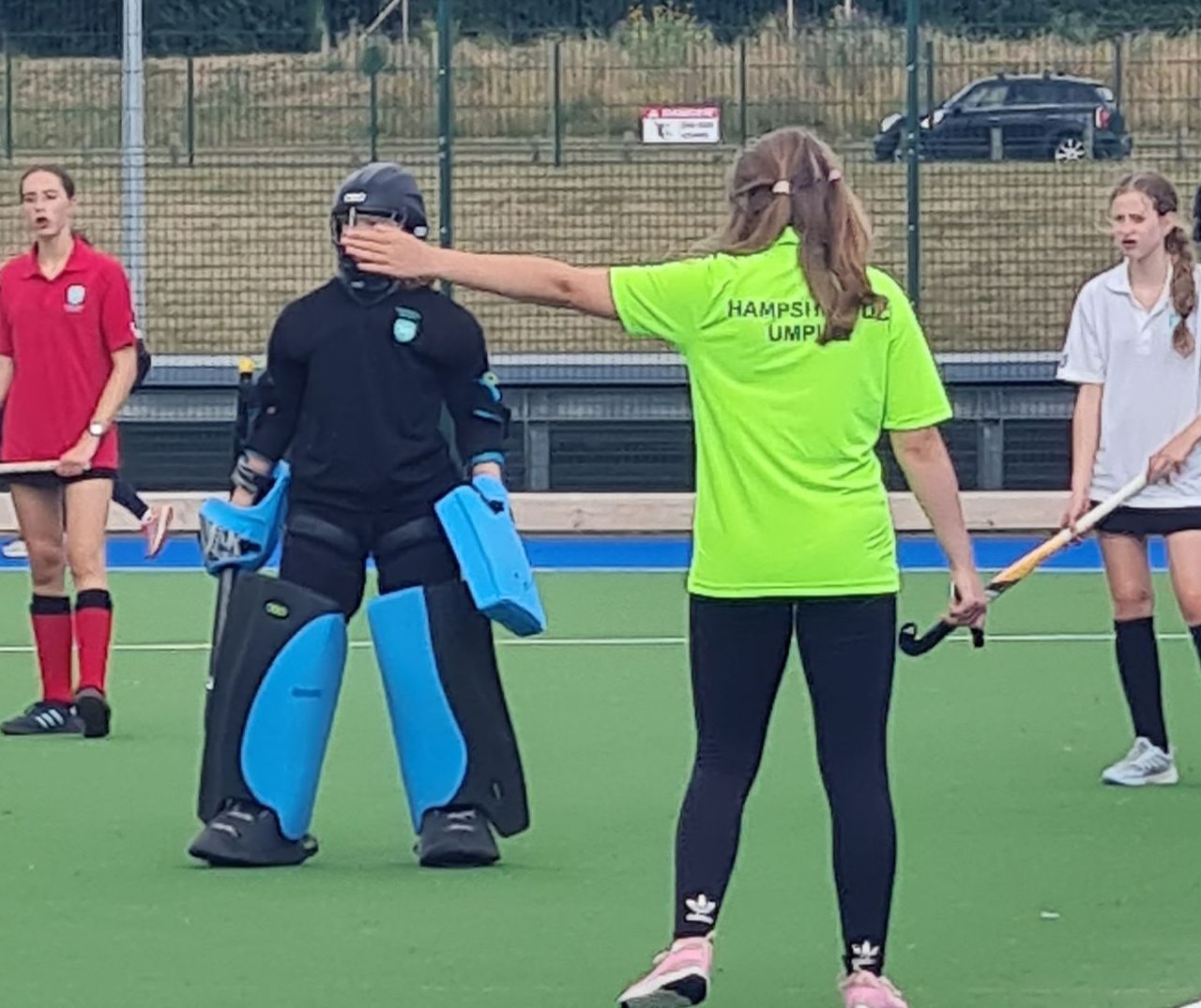A young umpire in a green shirt on a hockey pitch