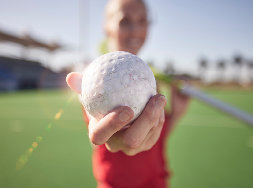 A woman is holding a hockey ball in her hand on a field.