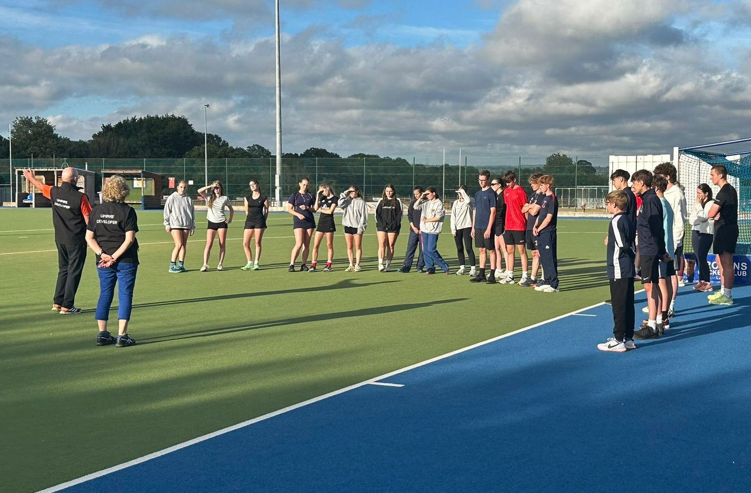 A group of young people are standing on a hockey pitch at the Hampshire DC Young Umpire Theory Eveni
