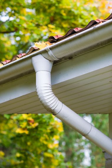 a close up of a white gutter on a roof with leaves on it .