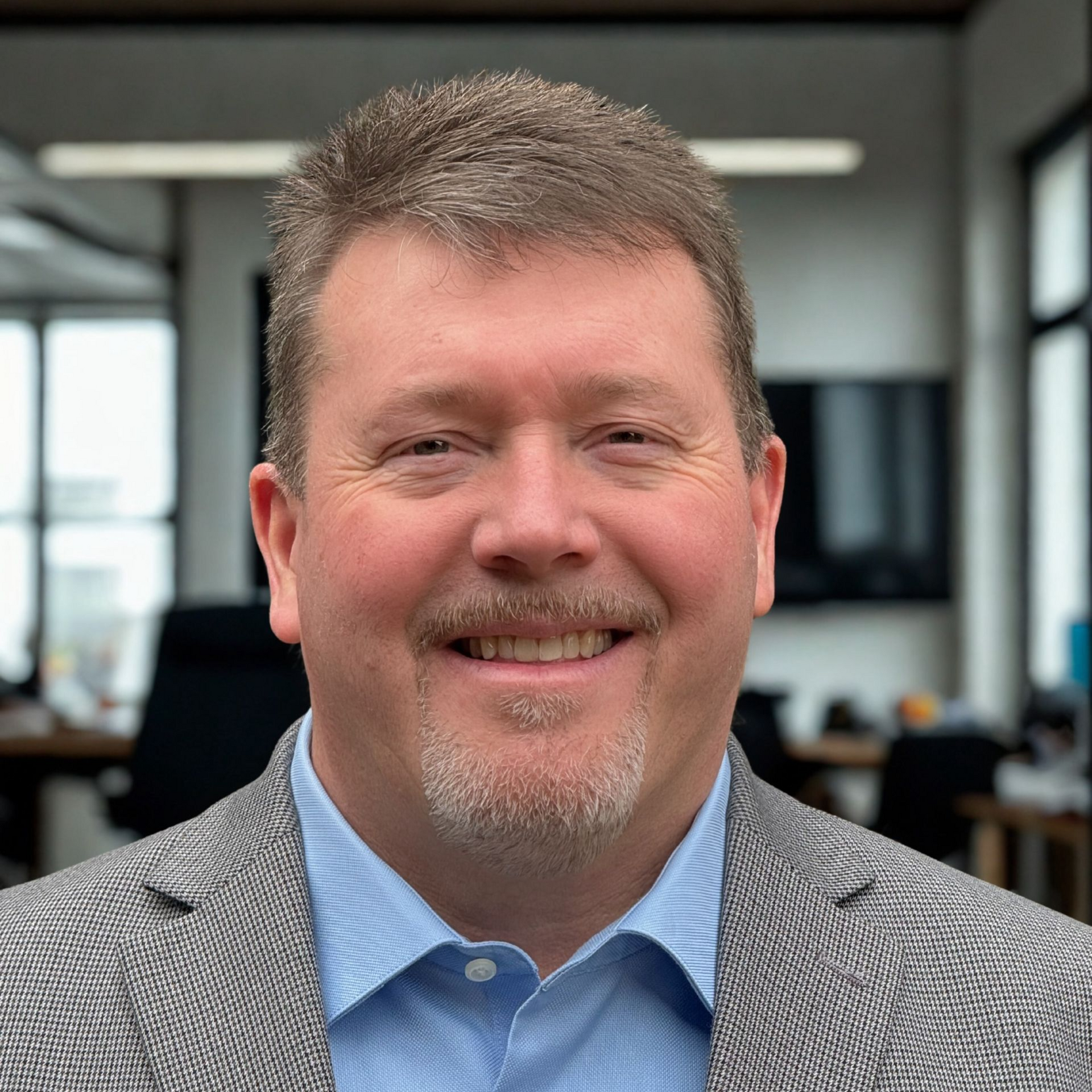 Man in a suit smiles, inside office.
