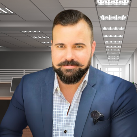 Man in blue suit, groomed beard, and mustache, set in an office hallway.