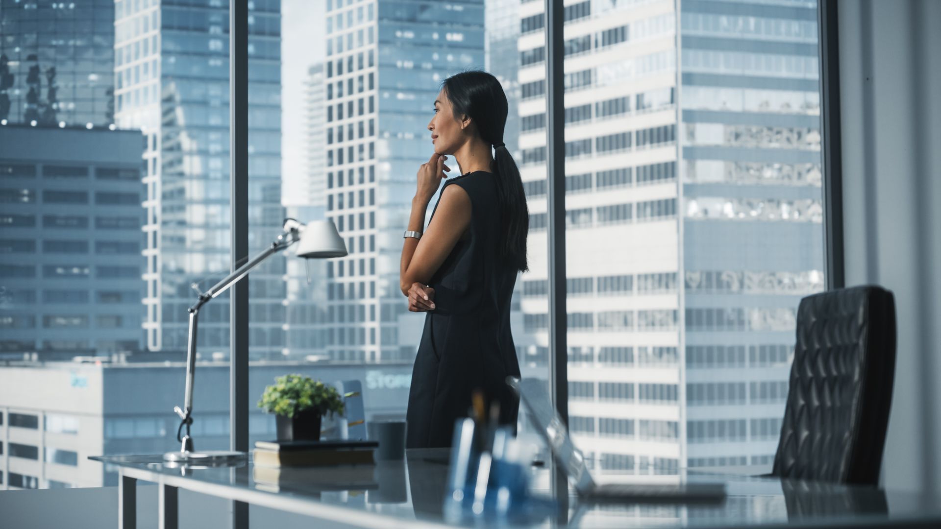 A woman is standing in front of a window in an office talking on a cell phone.