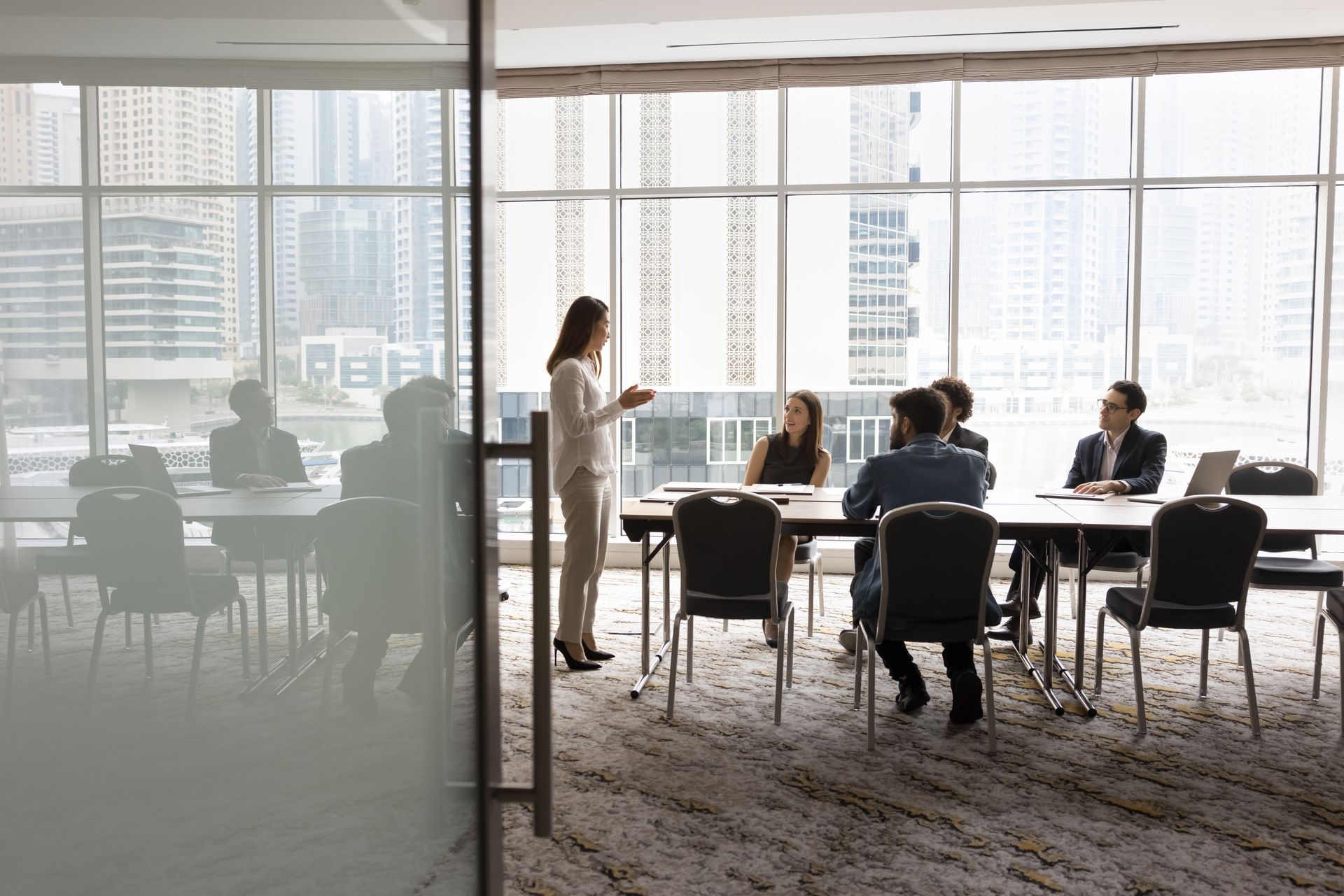 Woman leading a business meeting in a bright conference room with large windows, city view.