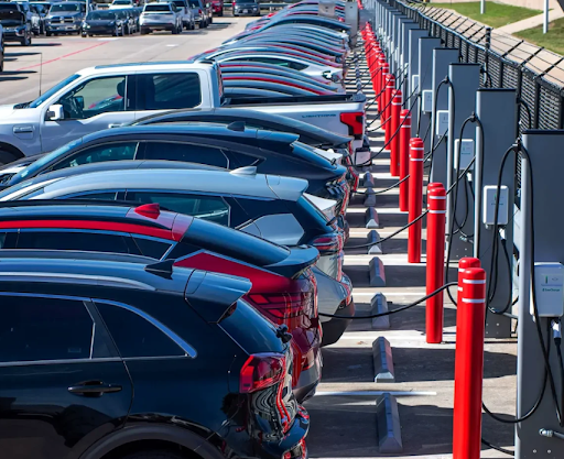 Cars parked and charging at an outdoor electric vehicle charging station, with red bollards and charging cables.