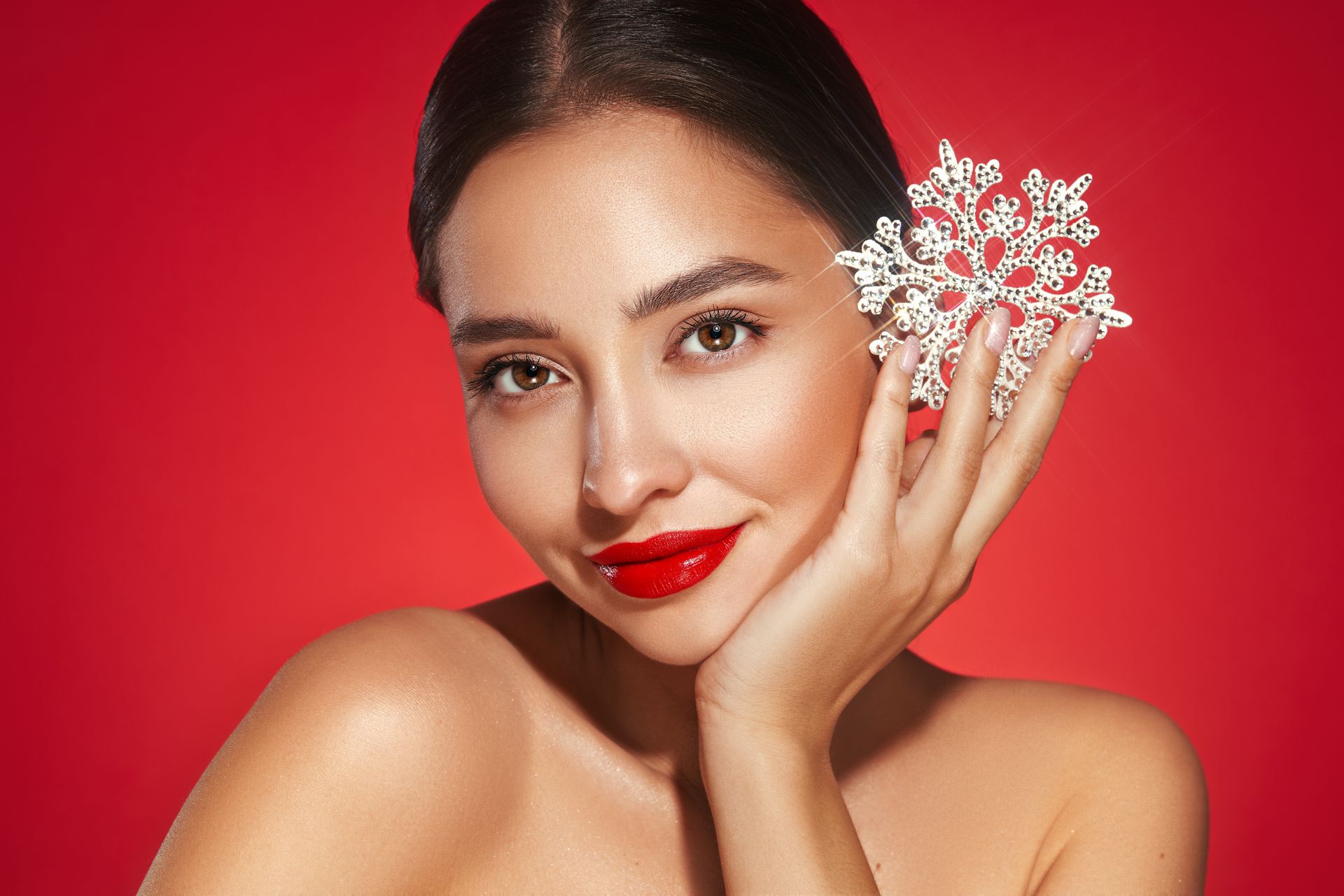 Woman with red lipstick holding a snowflake against her face, red background.