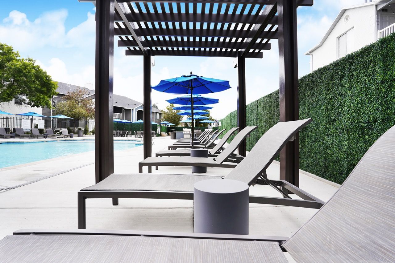 Outdoor community at Woodgate pool area with lounge chairs, blue umbrellas, and a pergola.