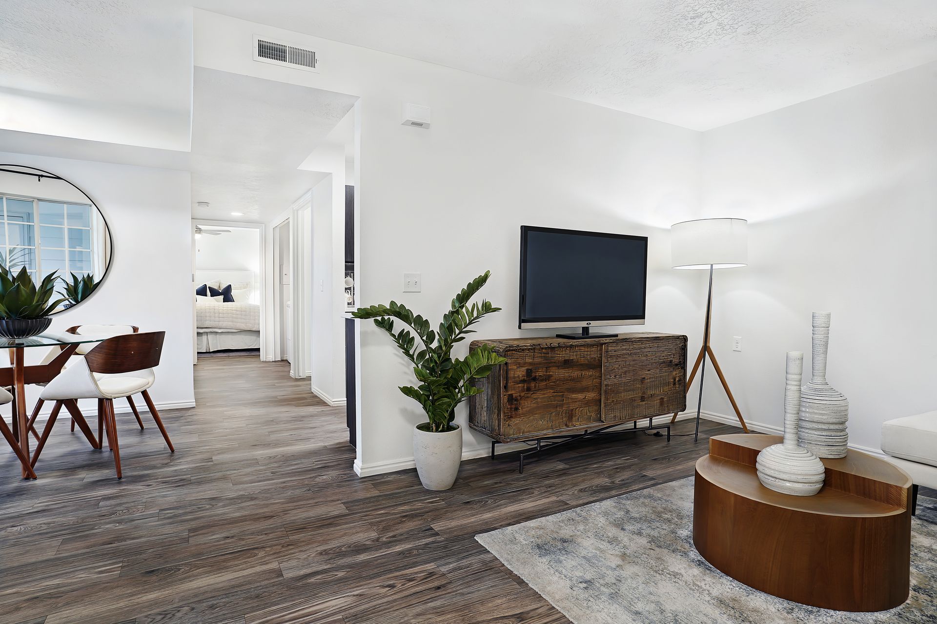 Open living room with hardwood floors, a TV on a rustic console, plant, and round coffee table at Woodgate.
