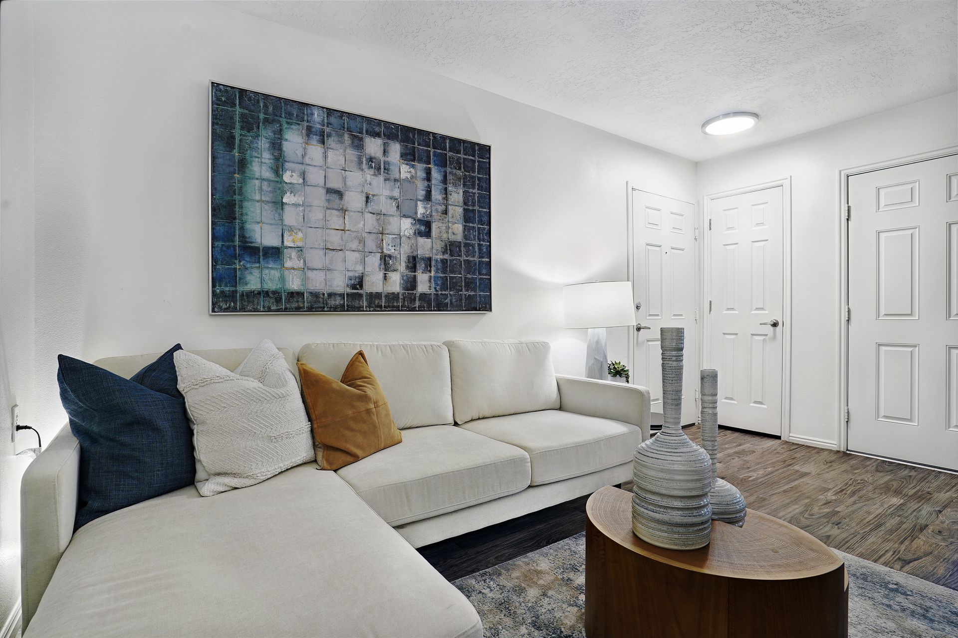 Bright living room in a modern apartment with a white sectional sofa, throw pillows, and abstract wall art at Woodgate.