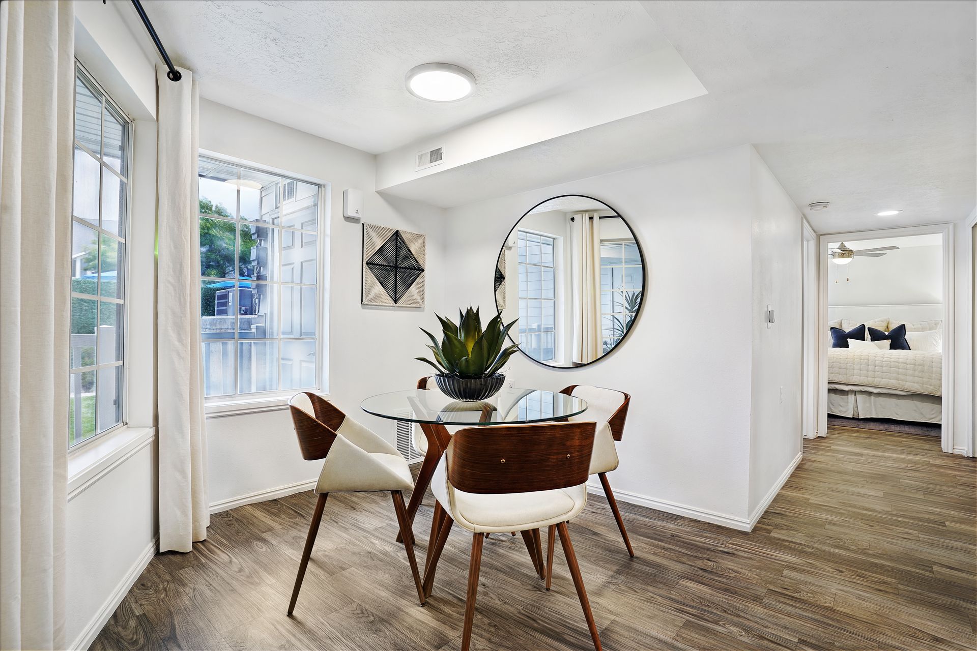 Bright apartment dining area with a round glass table, wooden chairs, and a doorway to the bedroom at Woodgate.