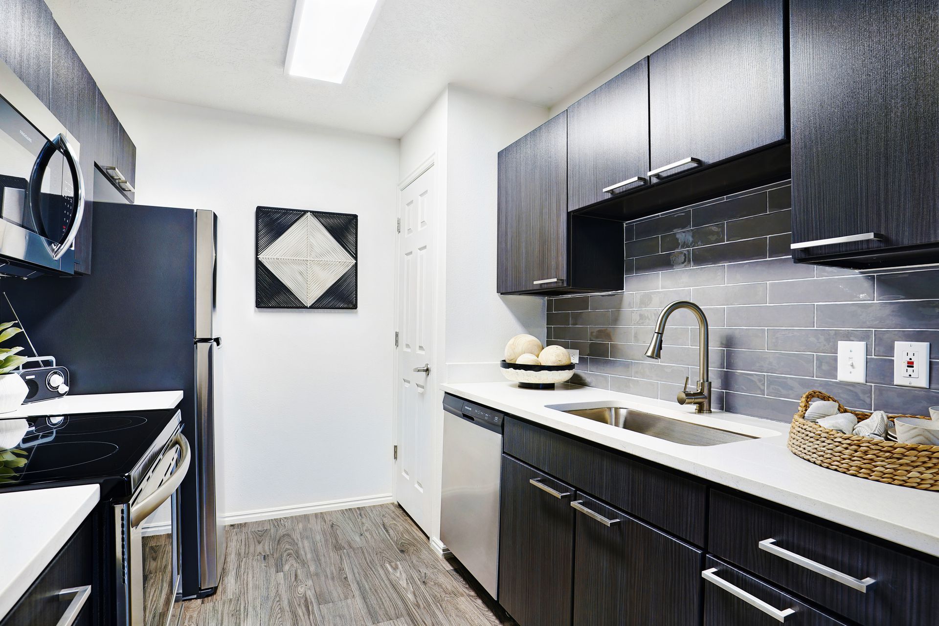 Modern apartment kitchen with dark cabinets, stainless appliances, and gray subway backsplash at Woodgate.