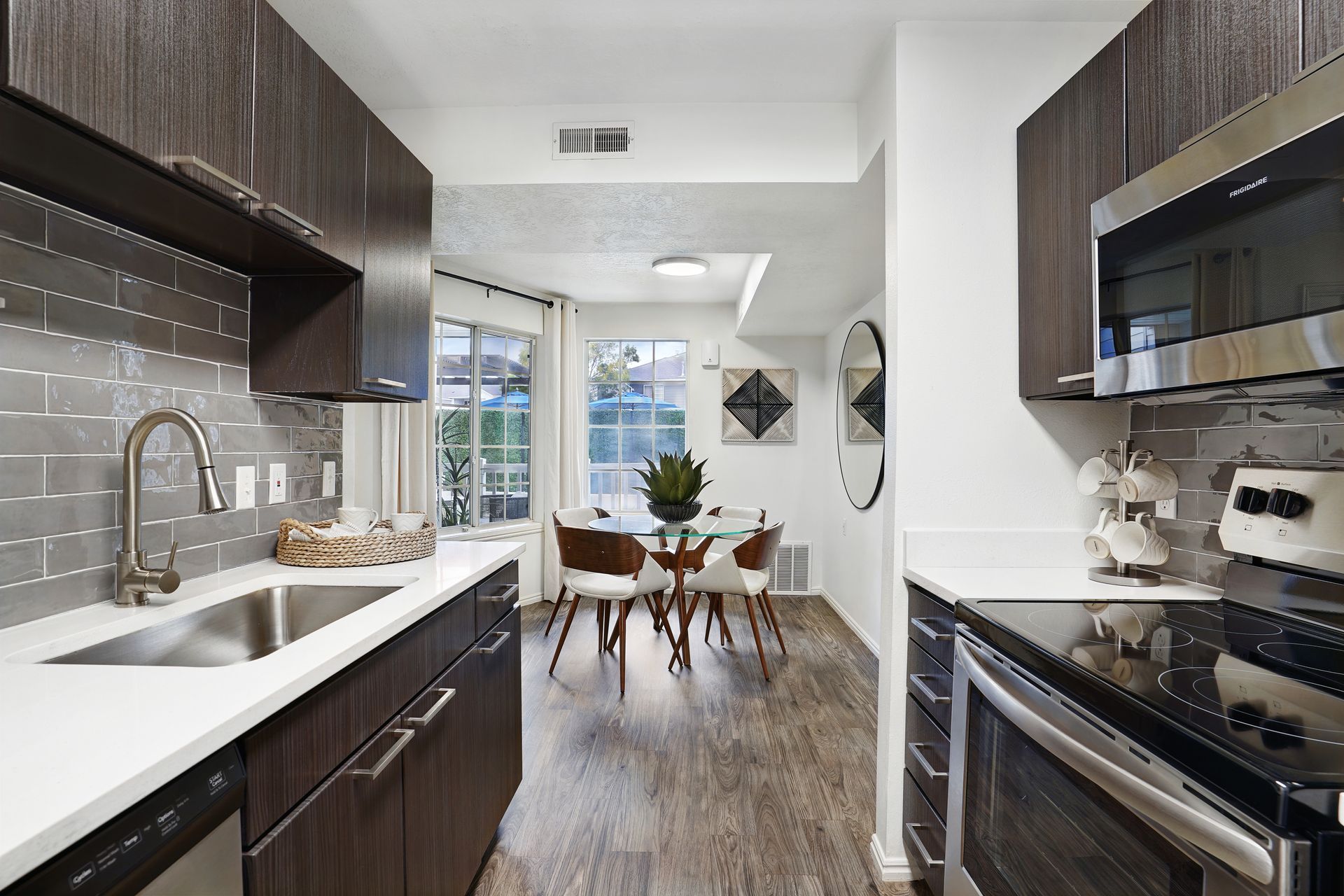 Modern apartment kitchen with dark wood cabinets, stainless steel appliances, and a glass dining table.