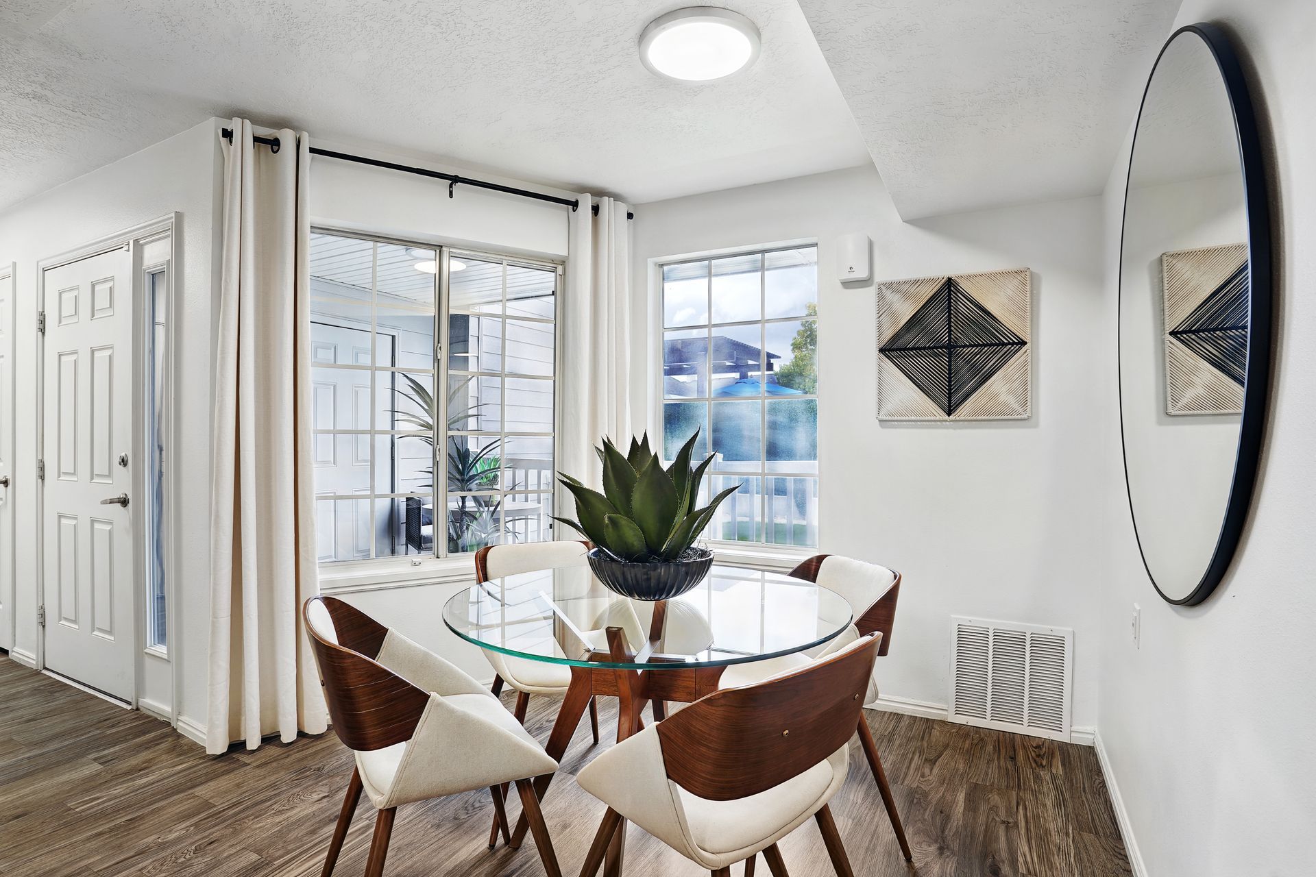 Dining area with a round glass table, four chairs, plant centerpiece, and a large window.