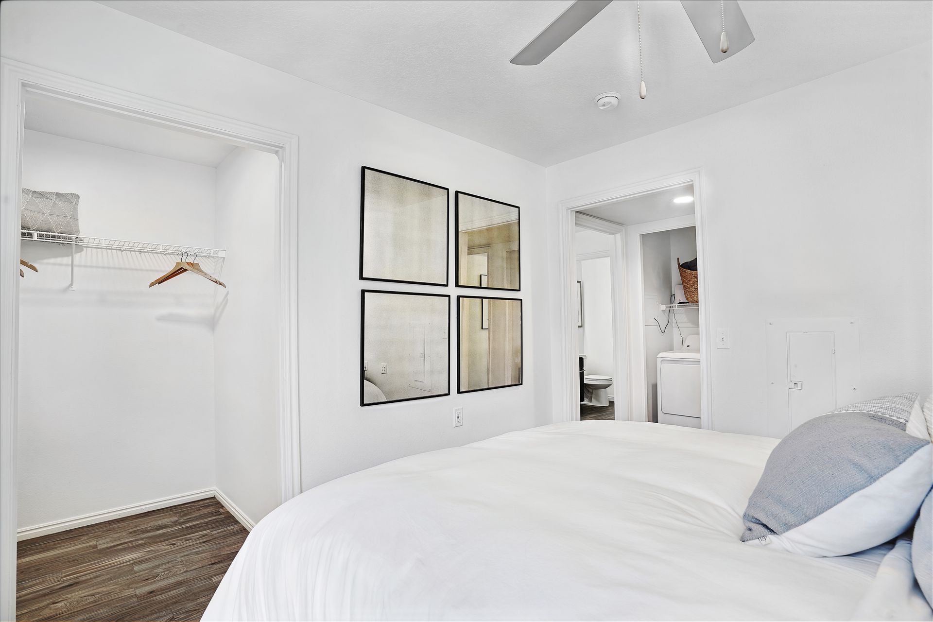 White bedroom with an open closet, bed in foreground, and doorway to the laundry area at Woodgate.
