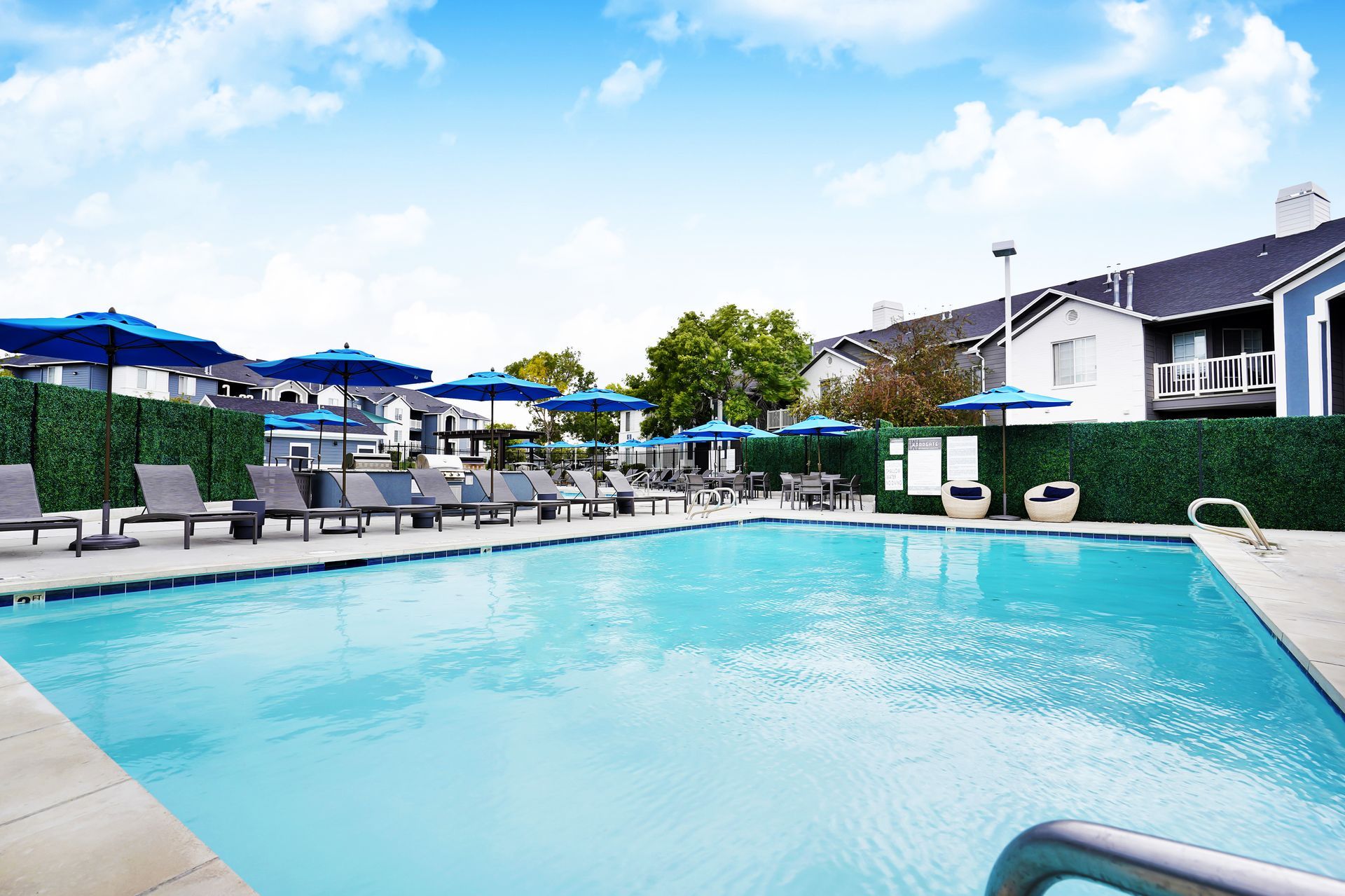 Outdoor pool at Woodgate with blue umbrellas and lounge chairs at a residential community.