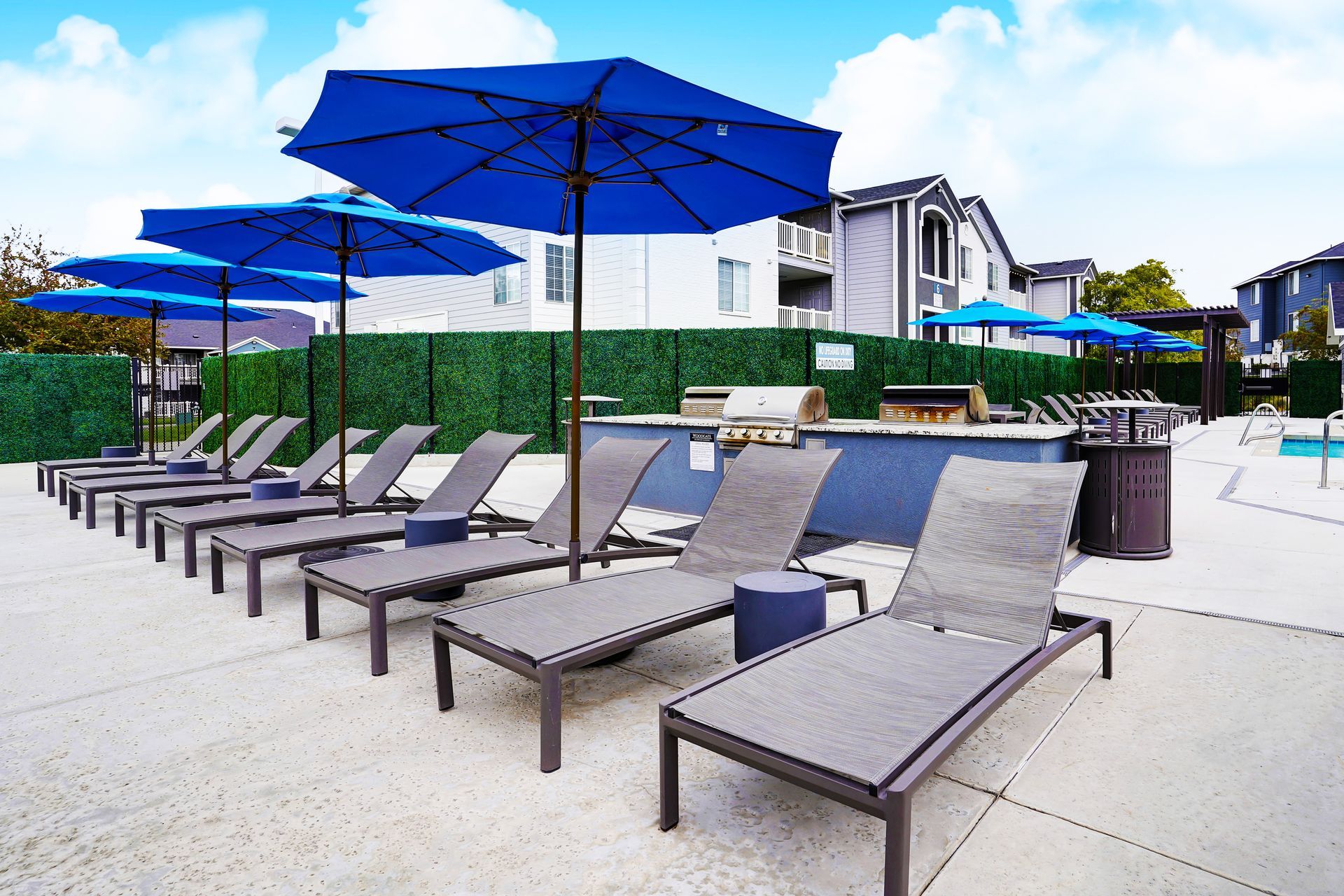 Outdoor apartment community pool at Woodgate area with blue umbrellas and lounge chairs.