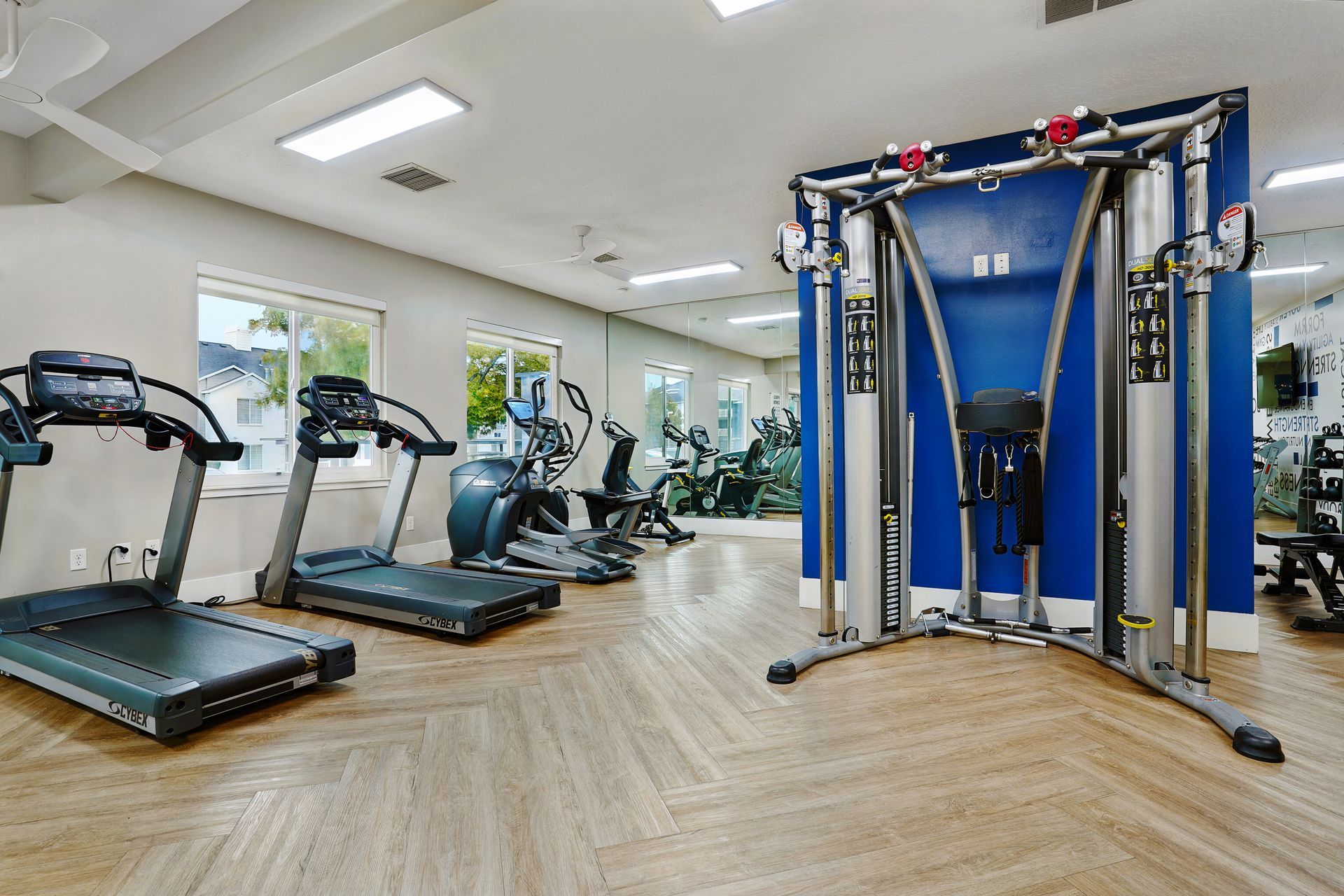 Bright on-site gym with treadmills, ellipticals, and a multi-station weight machine.