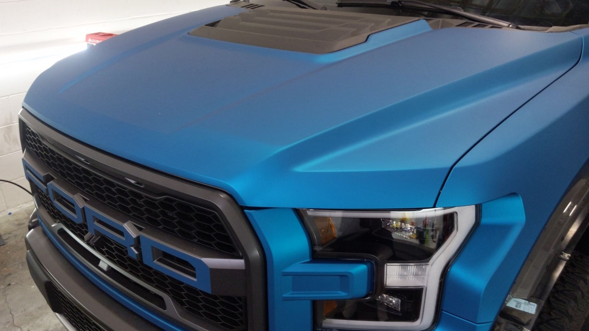 A blue ford raptor is parked in a garage.