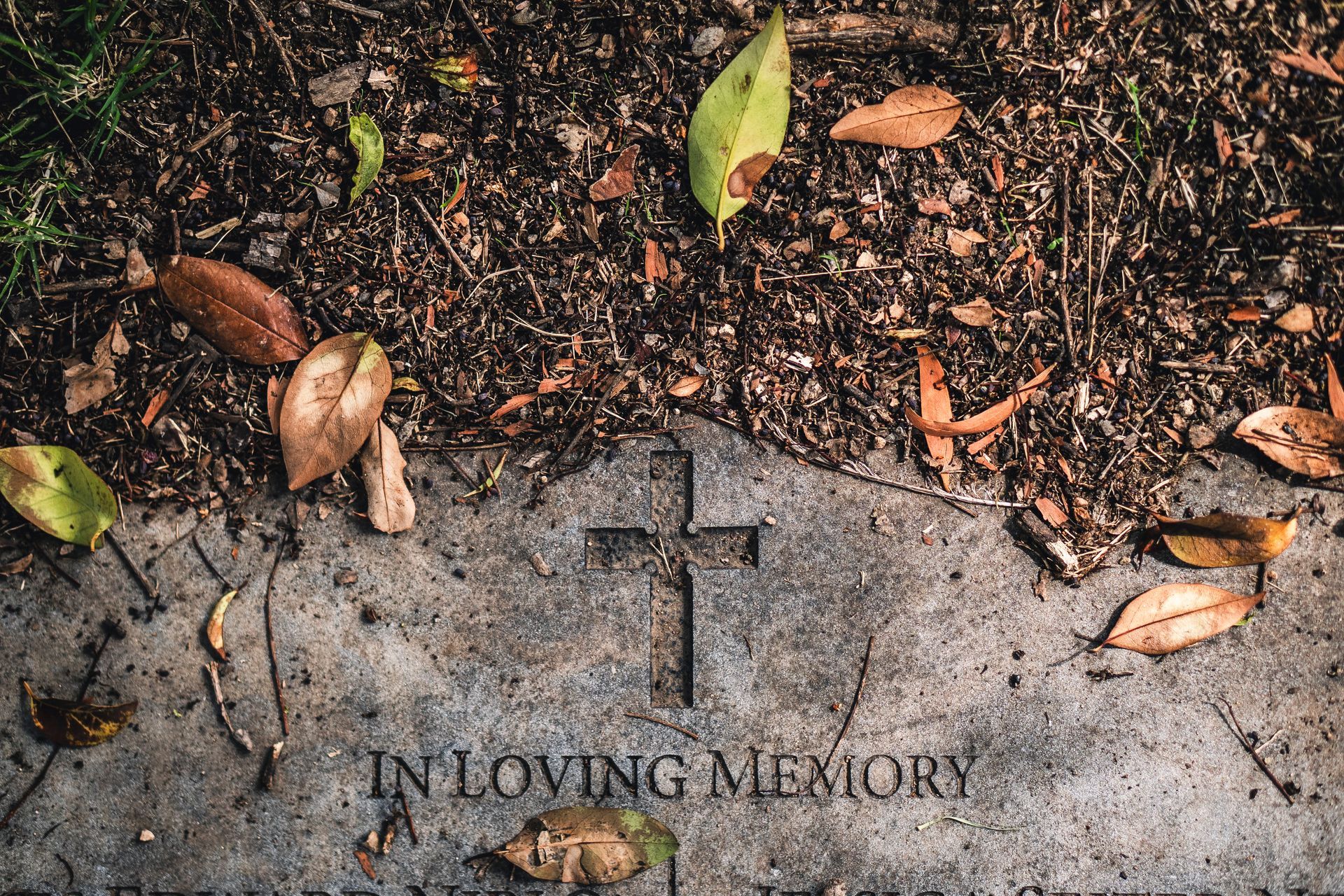 A grey stone grave marker with an engraved cross and the words