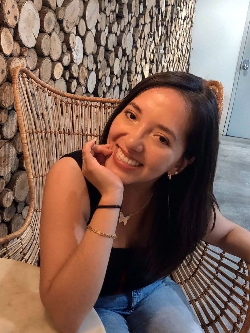 A woman is sitting in a wicker chair and smiling.