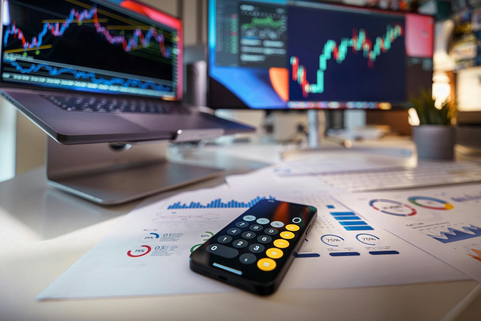 A calculator is sitting on a desk next to a laptop and two monitors.