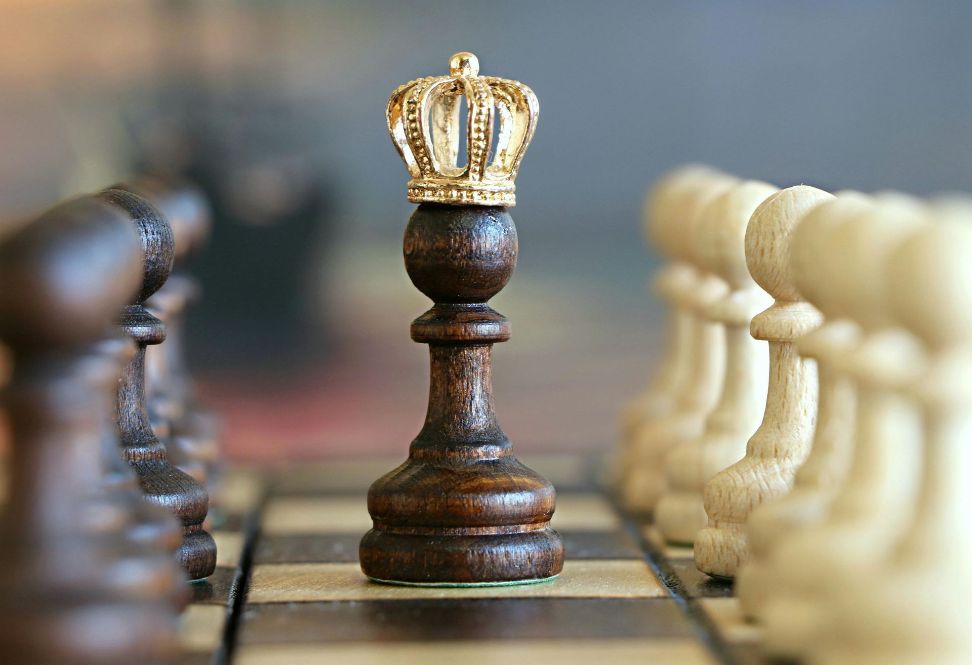 A wooden chess piece with a crown on top of it is on a chess board.