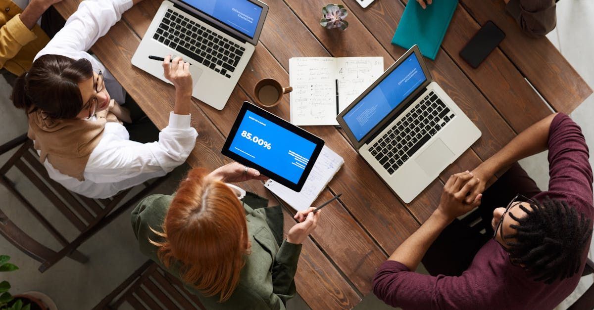 A group of people are sitting around a table with laptops and a tablet.