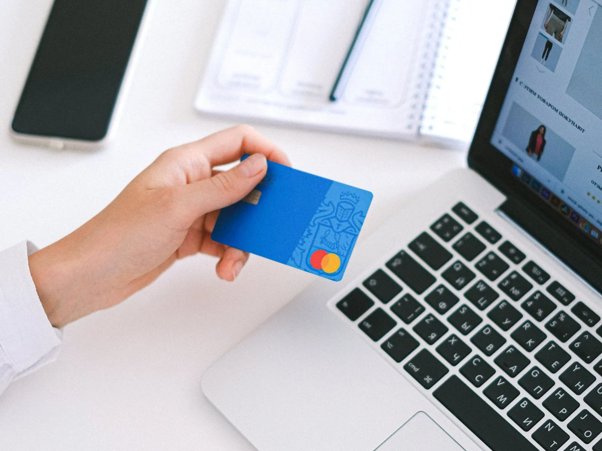 A person is holding a credit card in front of a laptop computer.