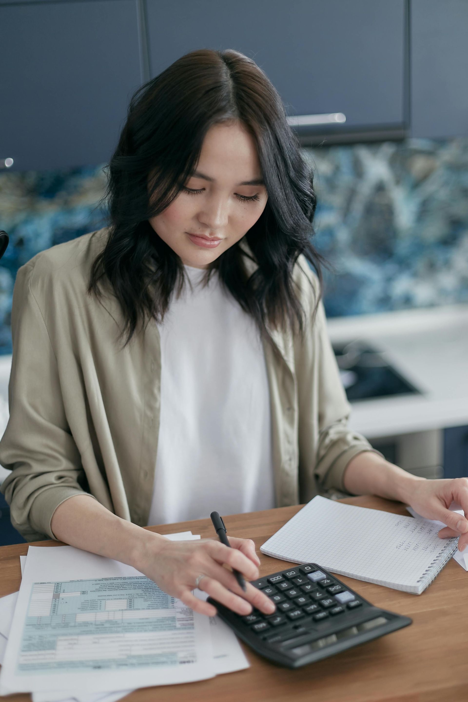 A woman is sitting at a table using a calculator.