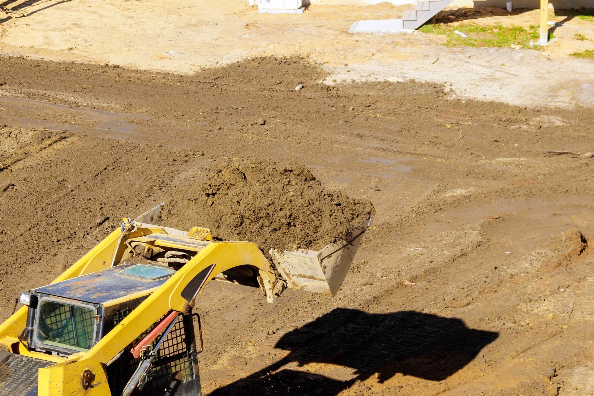 Yellow skid steer with dirt in its bucket on a construction site.