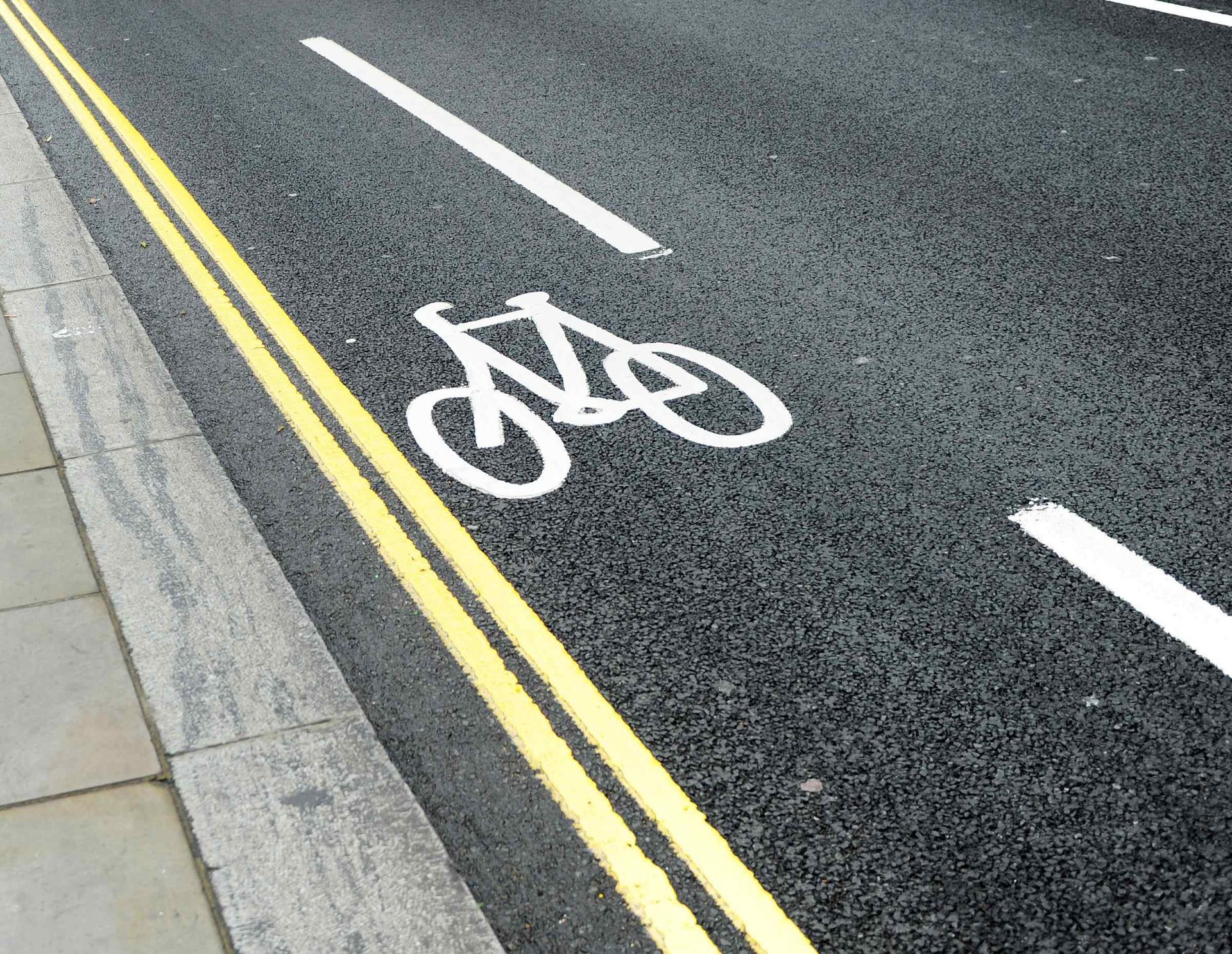 Asphalt road with yellow and white markings; a bicycle lane symbol.