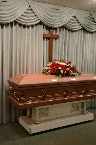 Wooden casket with floral arrangement and cross at a funeral.