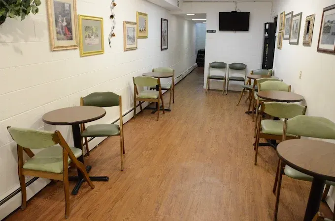 Waiting room with small tables, green chairs, framed pictures, and a TV.