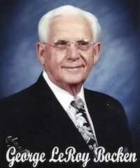 George LeRoy Bocken, elderly man in suit, glasses, smiling, against a blue background.