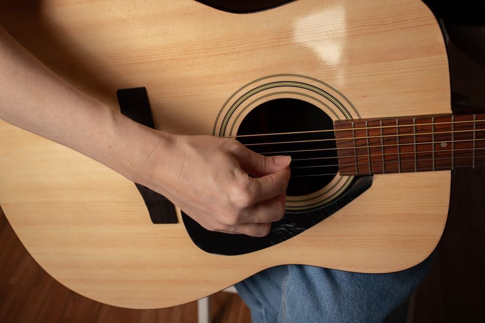 A person playing an acoustic guitar, strumming the strings with their right hand. Close-up view.