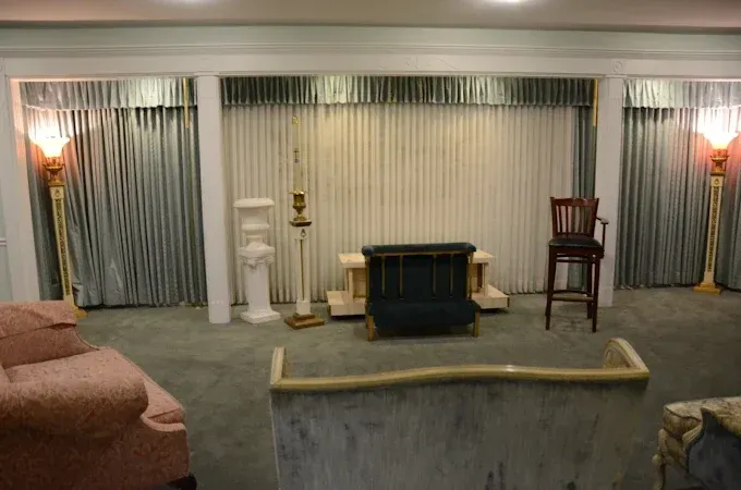 A formal room with a light blue color scheme, featuring curtains, seating, and decorative lighting.