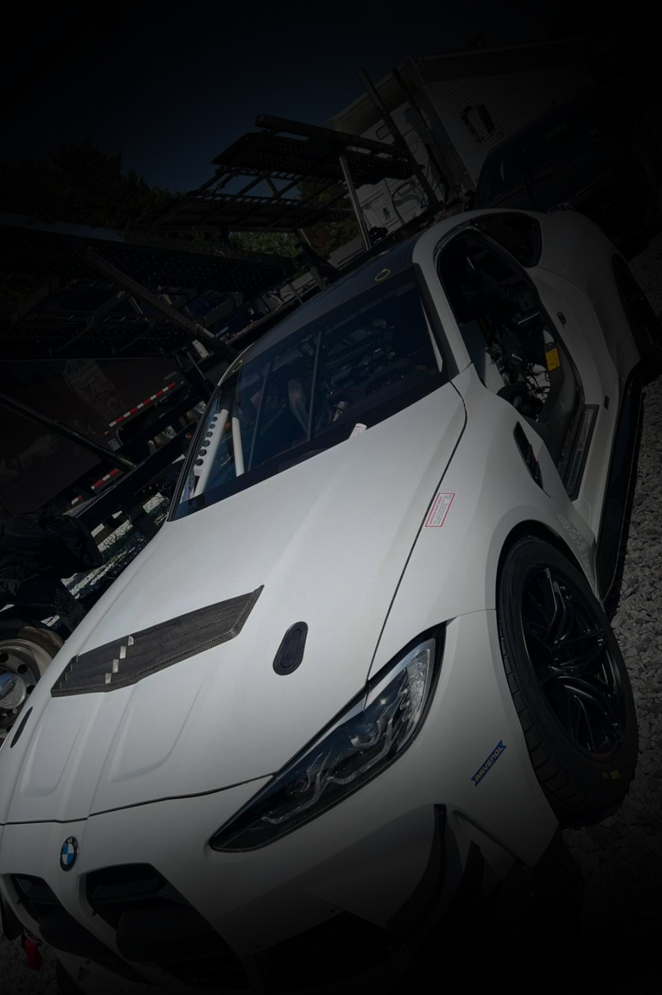 A white BMW racing car parked outdoors, featuring a vented hood and black wheels in low-light conditions.