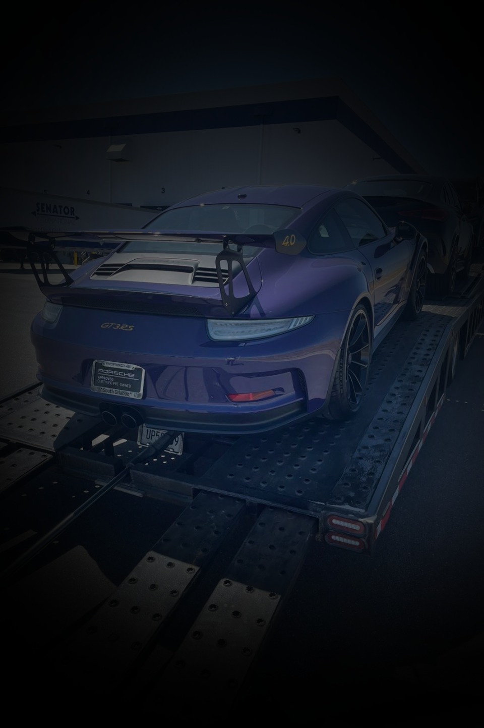 A dark purple Porsche 911 GT3 RS secured on a flatbed car hauler trailer.