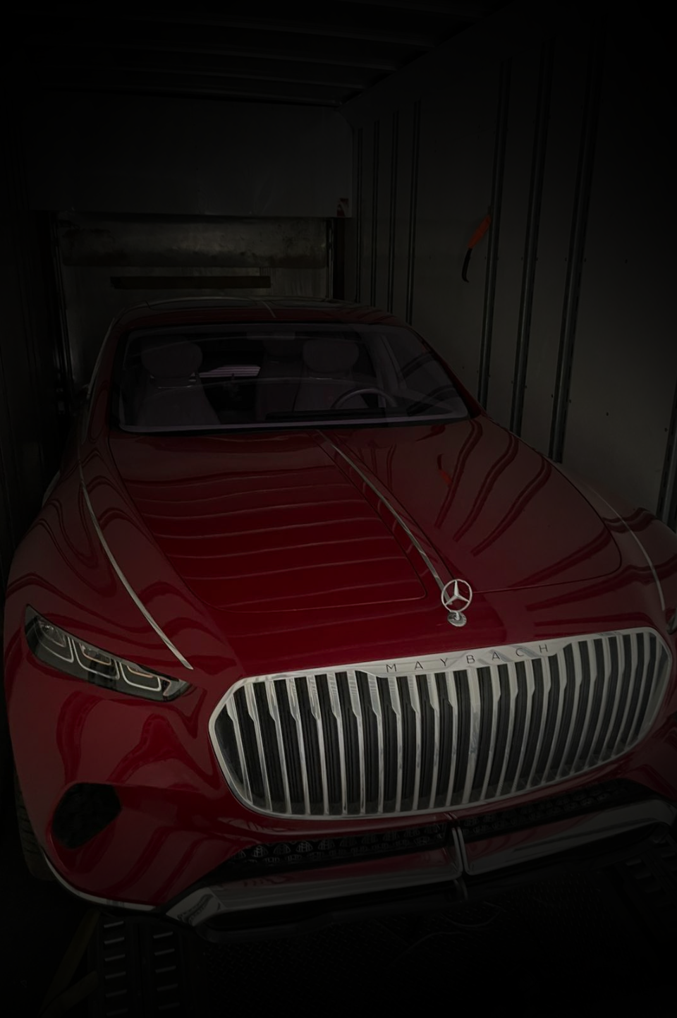 A red Mercedes-Benz with a prominent grille parked inside a dark trailer.