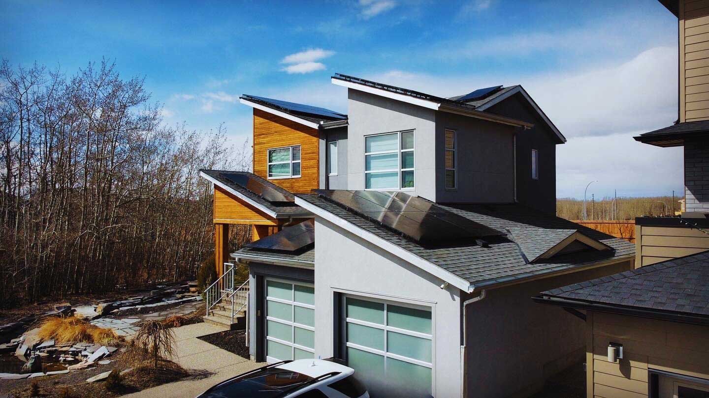 Modern homes with angled roofs, solar panels, and garage doors, set against a blue sky with some trees.