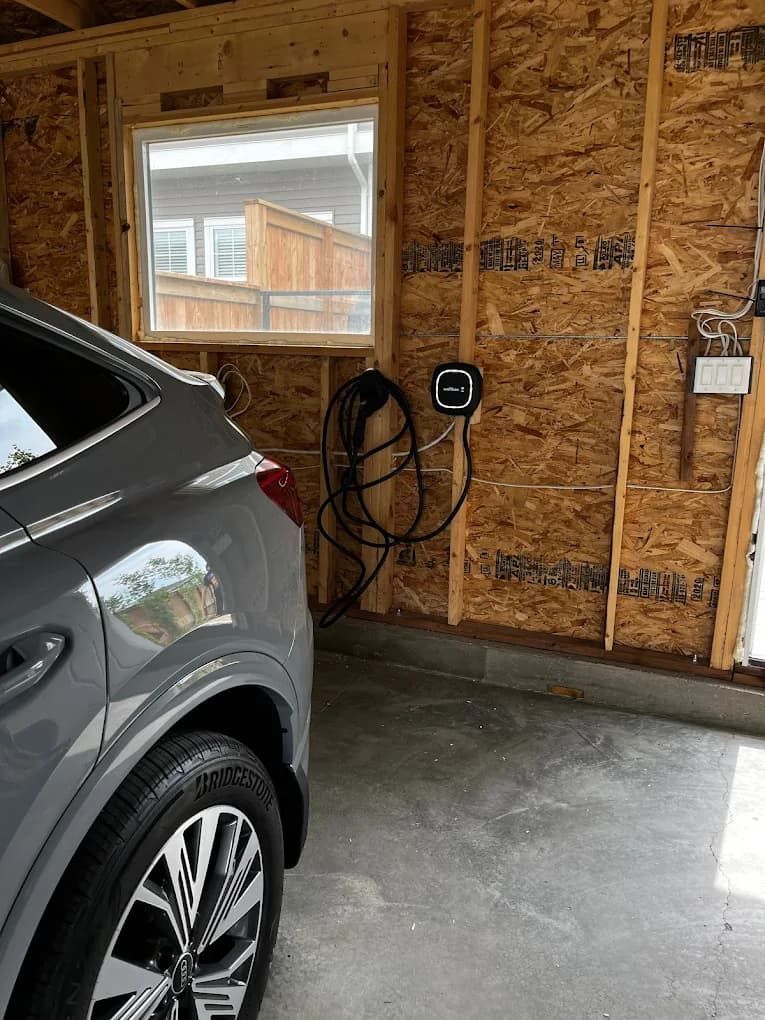Gray car parked in a garage next to an EV charger on a wood-paneled wall.