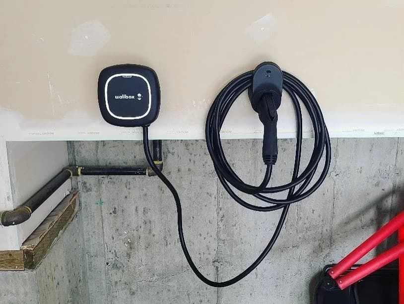 Black electric vehicle charger mounted on a garage wall, cable coiled nearby.