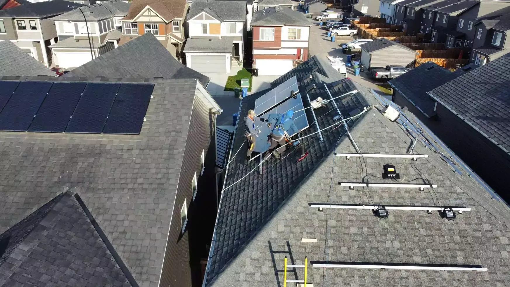 Rooftop solar panel installation. Workers on a sloped roof with panels, equipment, and residential neighborhood.