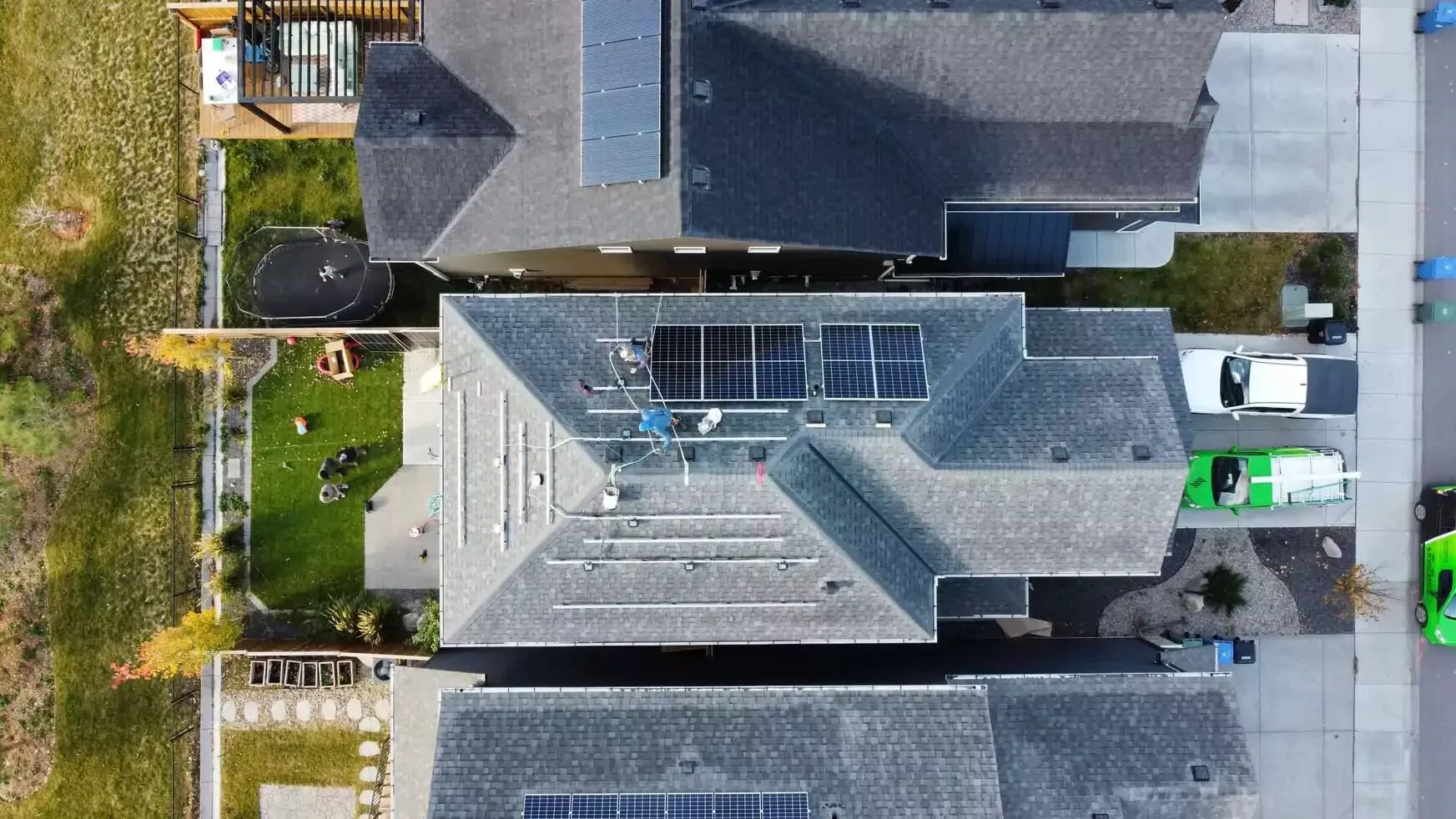 Overhead view of houses with solar panels on rooftops, green lawns, and a street.