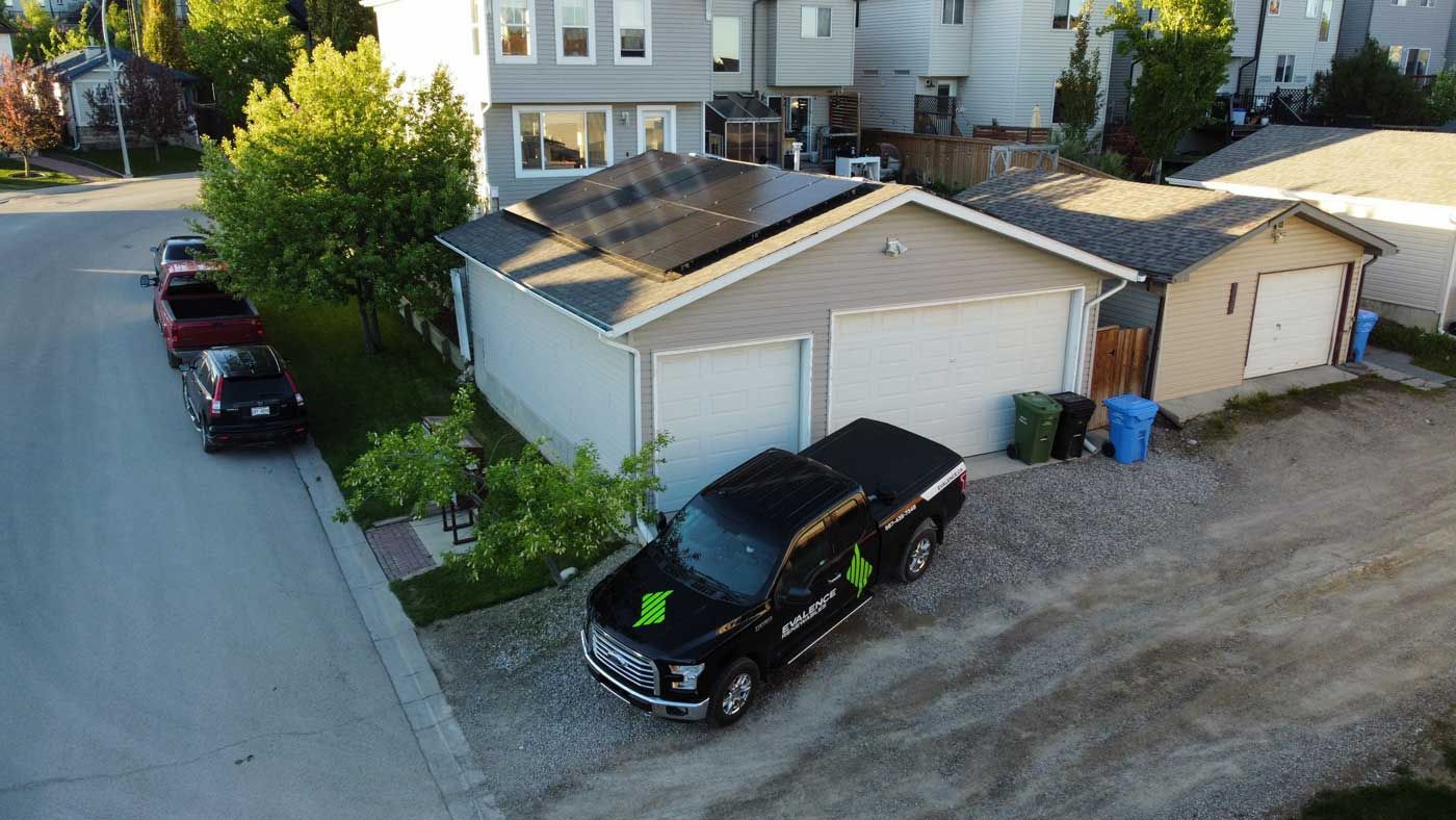 Black Evalence truck parked in front of a garage with solar panels on the roof.