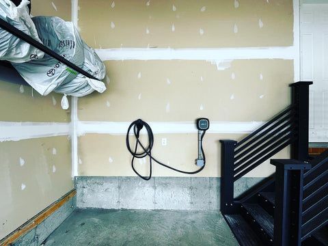 Electric vehicle charger mounted on a garage wall, near a set of stairs.