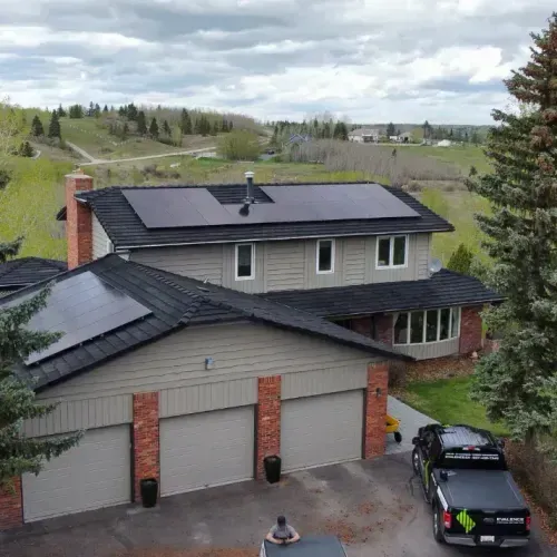 House with solar panels on the roof, gray siding, brick accents, and a black pickup truck parked in the driveway.