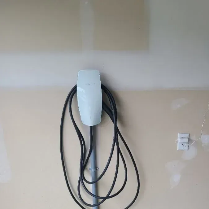 A white electric vehicle charger is mounted on a beige garage wall with a coiled black charging cable.